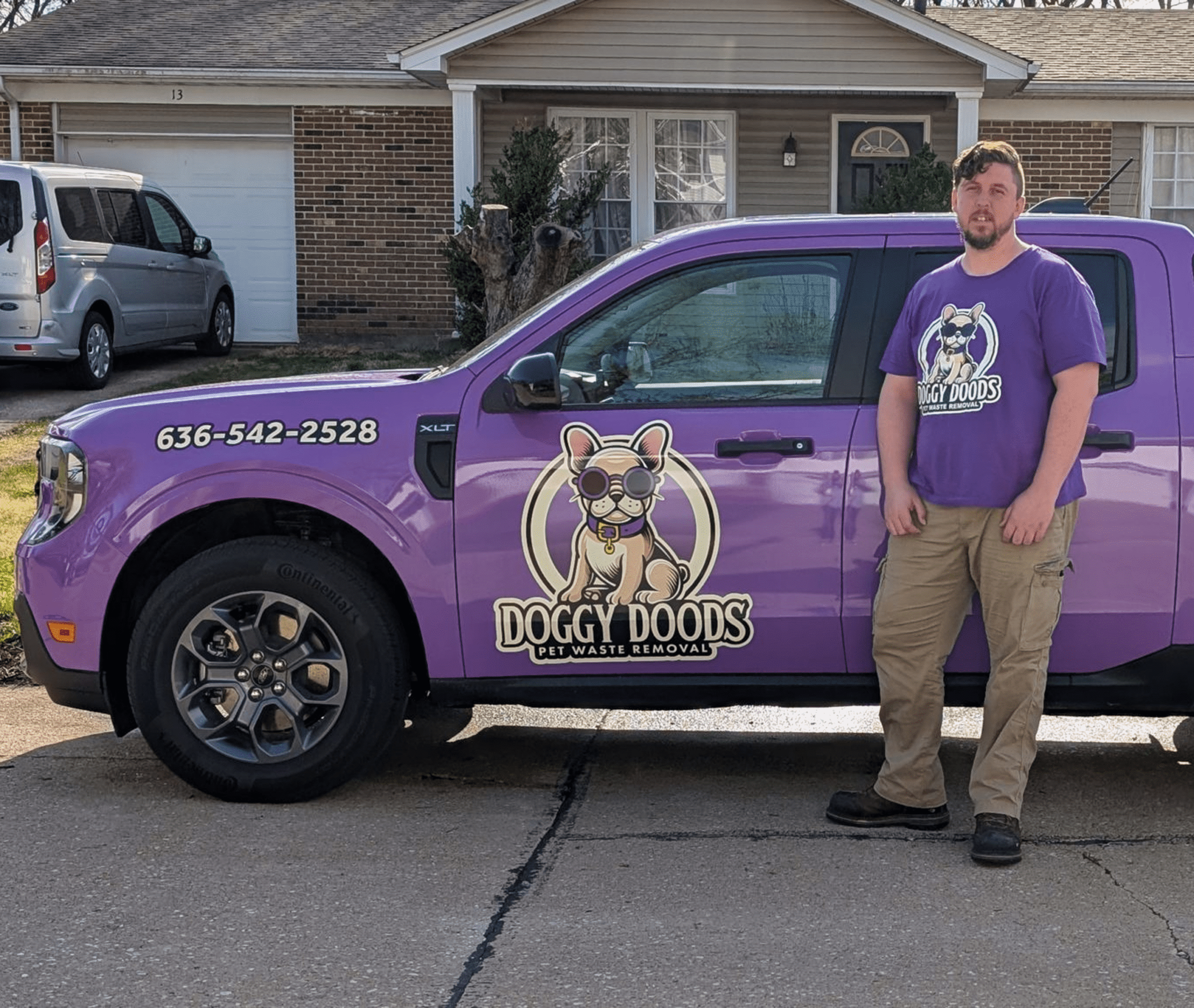 Doggy Doods owner standing beside purple truck with French Bulldog logo in front of a St. Charles County home.