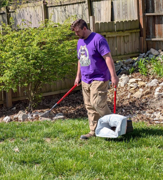Doggy Doods owner scooping dog poop in yard near garden