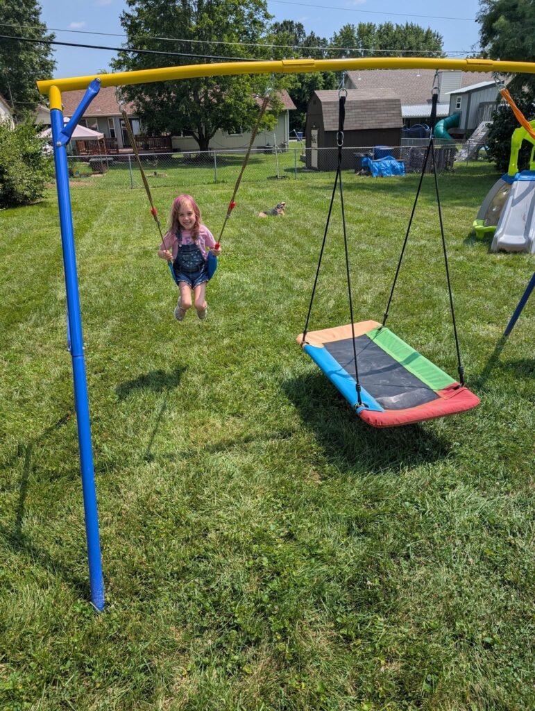 Doggy Doods owner's daughter swinging and dog, Nova, playing in the yard